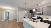 Located at 12810 Cypress Cape Cir in Fort Myers, FL, this 1-bedroom, 1-bathroom unit offers a thoughtfully designed single-floor layout with modern finishes throughout. The open-concept living and kitchen area is anchored by a striking kitchen island with a crisp white quartz countertop, undermount sink, and elegant pendant lighting. Dark espresso cabinetry extends floor-to-ceiling, complemented by a white subway tile backsplash and a full suite of stainless steel appliances, including a refrigerator, range, and microwave. Light wood-look flooring runs throughout the main living areas, creating a warm, cohesive aesthetic. The spacious living room features neutral warm-toned walls and a large window that invites natural light and views of the surrounding greenery. The carpeted bedroom offers a comfortable retreat, complete with a ceiling fan, natural light from a wide window, and access to a dedicated closet. The bathroom is well-appointed with a full soaking tub and shower enclosed in white subway tile, paired with a modern vanity. A dedicated laundry room houses a full-size washer and dryer, adding everyday convenience to this well-rounded Fort Myers residence.