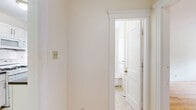 Located at 135 Washington St in Boston, MA, this two-bedroom, one-bathroom unit offers a practical and classic layout across a single floor. Warm-toned hardwood flooring runs throughout the main living areas and bedrooms, lending a timeless character to the space. The primary bedroom is generously sized, filled with natural light from multiple windows, and includes built-in closet storage behind classic white-paneled doors. The second bedroom also features hardwood floors and connects conveniently to the rest of the unit. The galley-style kitchen is efficiently designed, featuring white cabinetry with updated hardware, dark granite-style countertops, white subway tile backsplash, a gas range, and tile flooring — all oriented around a central window that brings in natural light. The bathroom is clean and classic, with white subway tile surround, a shower-tub combination, a vanity with mirror cabinet, and a window for ventilation. The entry hallway is tiled and includes an electrical panel, providing a functional transition into the home. Cast-iron radiators throughout provide efficient heating. The unit's bright, neutral palette and traditional architectural details make it a solid, well-structured home in the heart of Boston.