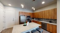 Located at 1001 W Rosedale St in Fort Worth, Texas, this single-story residence offers a cohesive modern design carried consistently throughout each space. The kitchen serves as a central highlight, showcasing warm wood cabinetry extending to the ceiling, a textured stone tile backsplash, and granite-topped countertops. Stainless steel appliances—including a full-size refrigerator, electric range, microwave, and dishwasher—provide full functionality. A granite-topped island with seating for multiple occupants anchors the kitchen and connects it to the living area. Pendant lighting fixtures add a stylish, contemporary touch overhead.

The living area features wood-look plank flooring, a wall-mounted television, and a sliding glass door fitted with vertical blinds that allows natural light to filter into the space. The bedroom offers multiple windows with blinds, providing ample natural light and a bright, airy atmosphere, complemented by the same wood-look flooring found throughout. The bathroom is finished with a granite vanity top, warm wood cabinetry, a large mirror with modern vanity lighting, and a tiled tub-shower combination, completing the consistent, polished aesthetic of the overall space.