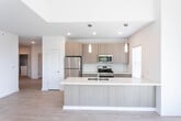 Located at 155 Smith St in Keasbey, NJ, this single-floor unit showcases a clean, contemporary design with light hardwood-style flooring throughout. The open-concept living and kitchen area is a standout feature, highlighted by soaring vaulted ceilings, recessed lighting, and large windows that flood the space with natural light and offer views of the surrounding greenery. A sliding glass door leads to a private balcony, further enhancing the airy feel of the living area.

The kitchen is thoughtfully designed with warm wood-toned cabinetry extending to the ceiling, a white subway tile backsplash, stainless steel appliances including a gas range, microwave, and refrigerator, and a large peninsula with a white quartz countertop, undermount sink, and stylish pendant lighting overhead.

The bedrooms are bright and well-proportioned, each featuring large windows with outdoor views and wall-unit climate control. At least one bedroom includes a dedicated walk-in closet with built-in shelving.

The bathrooms are finished with wood-toned vanities, dark quartz countertops, undermount sinks, and large mirrors. The primary bathroom features a glass-enclosed tiled walk-in shower, while the secondary bathroom is equally well-appointed with a similar aesthetic.