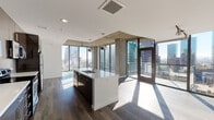 Located in the heart of Downtown Los Angeles, this contemporary high-rise unit at 801 S Hope St delivers a striking blend of industrial-modern design and urban sophistication. Expansive floor-to-ceiling windows wrap around the living areas, flooding the space with natural light and framing breathtaking panoramic views of the Los Angeles skyline. Exposed concrete ceilings and structural columns add an authentic industrial character that contrasts beautifully with the clean white walls and smooth hardwood flooring throughout.

The open-concept kitchen is a standout feature, anchored by a sleek white island with an integrated sink and pendant lighting overhead. Dark espresso cabinetry lines the walls, complemented by stainless steel appliances, a tile backsplash, and ample counter space — making it as functional as it is visually striking. The living area extends seamlessly from the kitchen, offering generous open space with dramatic city views on multiple sides.

The bedrooms benefit from the same floor-to-ceiling glazing, with ceiling fans and continued hardwood flooring. The bathrooms are finished with large-format tile, dark vanity cabinetry, white quartz countertops, and generous mirror space. The primary bath includes a soaking tub, a tiled walk-in shower, and access to a walk-in closet, delivering a refined and practical retreat within this vibrant urban setting.