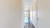 Located on Chapel Street in the heart of New Haven, CT, this modern single-floor unit offers a clean, contemporary design throughout. The space is defined by gleaming, highly polished dark hardwood-style flooring that reflects natural light and lends a polished feel to every room.

The open kitchen is well-appointed with rich dark wood cabinetry, granite countertops, a white tile backsplash, and a full suite of stainless steel appliances including a gas range, built-in microwave, dishwasher, and refrigerator — providing both style and functionality.

A wide hallway connects the living area to the rest of the unit, lined with multiple closet doors for generous storage. The main living area is bright and airy, featuring a large floor-to-ceiling window that frames views of the New Haven skyline and surrounding greenery, flooding the room with natural light. Track lighting along the ceiling adds a modern, gallery-like touch.

The bathroom is finished with large-format gray ceramic floor tiles, a sleek floating vanity with dark cabinetry, and a full-size tub and shower combination with clean white tile surround and a glass panel. Throughout the space, a neutral white palette and minimalist design create a calm, versatile ambiance well-suited for a variety of uses.