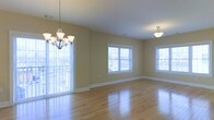 This well-appointed single-floor space offers a welcoming and airy atmosphere defined by clean lines and thoughtful design. The main living area is finished with rich, honey-toned hardwood flooring that runs throughout, reflecting natural light and adding warmth to the interior. Walls are painted in a soft, neutral yellow tone that complements the light wood floors and white trim, creating a cohesive and inviting aesthetic.

Lighting is a standout feature, with a classic multi-arm chandelier serving as an elegant focal point, paired with an additional ceiling-mounted pendant fixture to ensure the space is well-lit. Multiple windows fitted with horizontal blinds allow generous amounts of natural light to fill the room, while a large sliding glass door with vertical blinds provides direct access to an outdoor area and further brightens the interior.

The white baseboards and clean wall finishes contribute to a polished, move-in-ready appearance. The open layout of the main living area offers generous space for a variety of furniture arrangements, making it highly versatile. Overall, the space combines classic design elements with practical functionality, offering a bright, comfortable, and welcoming environment suitable for everyday living.