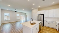 Located at 550 NW E. Crawford Ave in Fate, TX, this single-story home offers a thoughtfully designed open-concept floor plan with three bedrooms and three full bathrooms. The heart of the home is a bright, combined kitchen, dining, and living area centered around a large white kitchen island with an undermount sink and matte black fixtures. White shaker cabinetry, stainless steel appliances, recessed lighting, and light hardwood-style flooring create a clean, modern aesthetic throughout the main living spaces. The spacious living room receives generous natural light through multiple windows and a sliding glass door, and features a ceiling fan overhead. Bedrooms are finished with plush carpet and panel-style doors, lending a quiet, comfortable feel. The primary bedroom includes its own en-suite bathroom, which features a frameless glass-enclosed walk-in shower with tile surround and built-in shelving. A dedicated laundry room houses a full-size washer and dryer with overhead shelving. Additional conveniences include a pantry, four closets, and two hallways. The backyard is enclosed by a cedar privacy fence with stone border landscaping, offering a well-maintained lawn and a covered patio area.