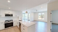 This well-appointed two-bedroom, two-bathroom residence spans two floors and offers a clean, contemporary design throughout. The open-concept living and dining areas flow seamlessly into a stylish kitchen, which features crisp white shaker cabinetry, quartz countertops, stainless steel appliances including a gas range and built-in microwave, and a large center island with pendant lighting — ideal for both everyday cooking and entertaining. Large windows and a glass exterior door in the living area flood the space with natural light and frame pleasant outdoor views of surrounding greenery.

Light wood-look flooring runs through the main living spaces, complementing the bright white walls and modern black hardware fixtures found throughout. A wide hallway with built-in closet storage connects the bedrooms, each of which features plush carpet, roller shade windows with outdoor views, and generous proportions. The primary bedroom includes a ceiling fan and its own dedicated closet. Both bathrooms are finished with white cabinetry, quartz vanity surfaces, and clean-lined mirrors. The overall aesthetic is modern and minimalist, creating a bright, airy atmosphere that feels open and move-in ready.