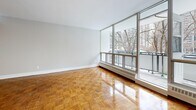This 2-bedroom, 1-bathroom unit offers a thoughtfully organized single-floor layout that makes excellent use of its space. The living area is a standout feature, highlighted by expansive floor-to-ceiling windows that flood the room with natural light and provide open views of the surrounding cityscape and mature trees. Warm, polished parquet flooring flows throughout the living areas and bedrooms, adding a timeless character to the interior. A balcony is accessible from the main living space, extending the sense of openness.

The kitchen is efficiently designed with a galley-style layout, featuring white cabinetry, light tile flooring, and a full suite of stainless steel appliances including a refrigerator, stove, built-in microwave, and dishwasher — providing a clean, modern aesthetic.

Both bedrooms continue the parquet flooring theme and are finished with neutral tones and double-door closets for ample storage. Each bedroom benefits from natural light, with the primary bedroom featuring its own window with outdoor views.

The bathroom is clean and functional, finished with white subway tile surrounding a full soaking tub with brushed nickel fixtures. The entrance and hallway connect all areas of the unit cohesively, completing a practical and comfortable layout suited for everyday living.