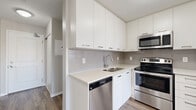 Located at 140 Main St W in downtown Hamilton, this modern condo offers a thoughtfully designed one-bedroom, two-bathroom layout with a versatile den, making efficient use of its well-proportioned floor plan. Light-toned laminate hardwood flooring flows consistently throughout, complementing the clean, neutral palette found in every room.

The open-concept living and dining area is bright and airy, with large sliding glass doors leading to a private balcony that allows natural light to fill the space. The kitchen is sleek and functional, featuring white flat-panel cabinetry extending to the ceiling for ample storage, a subway tile backsplash, quartz countertops, and a full suite of stainless steel appliances including a fridge, stove, microwave, and dishwasher.

The primary bedroom is a comfortable size, with tray ceiling detailing that adds architectural character, and direct access to the hallway connecting both bathrooms. Each bathroom is finished with clean, modern fixtures, including a dark wood vanity with white countertop, chrome hardware, and tile flooring. A dedicated den provides flexible space suitable for a home office or additional sleeping area. In-unit laundry adds everyday convenience, rounding out this well-appointed urban residence.