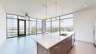 Located at 4040 Valley View Lane in Farmers Branch, TX, this contemporary single-floor residence offers 3 bedrooms and 2 bathrooms with a thoughtfully designed open-concept layout. The combined kitchen and living area is a standout highlight, featuring dramatic floor-to-ceiling black-framed windows that flood the space with natural light and frame impressive views of the surrounding cityscape. The kitchen is outfitted with flat-front wood-tone cabinetry, quartz countertops, a glass tile backsplash, stainless steel appliances, and a large central island with an undermount sink — ideal for both cooking and entertaining. The living area extends toward a glass-door balcony, reinforcing the connection to the outdoors. Wide-plank hardwood-style flooring runs throughout the main living areas, while plush carpeting provides comfort in the bedrooms. The spacious primary bedroom includes a generous walk-in closet with built-in shelving and hanging rods. The primary bathroom features a dual-sink vanity with wood-tone cabinetry, a large wall mirror, and an oversized glass-enclosed shower with marble-style tile surround. Additional bedrooms are bright and well-sized, each with ceiling fans and natural light. A dedicated laundry room and multiple closets throughout add to the home's practical functionality.