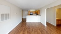 This single-floor residence offers a practical and well-organized layout designed for comfortable everyday living. The open-concept living area features warm wood-look flooring that extends through the common spaces, with a textured ceiling and large windows that allow natural light to fill the room. A door leads directly to an outdoor balcony, providing a pleasant extension of the living space.

The kitchen is positioned adjacent to the living area and is defined by a raised breakfast bar with seating, offering both functionality and a natural division of space. Warm oak cabinetry provides generous storage, while dark countertops and black appliances — including a refrigerator, electric range, and over-the-range microwave — create a cohesive, practical workspace.

The bedrooms feature plush carpeting and are brightened by large windows with blinds. Ceiling fans are installed in select rooms for added comfort. The bathrooms are finished with wood-look flooring, oak vanity cabinetry, and white fixtures. One bathroom includes a full bathtub and shower combination, while another features a wide vanity with a large mirror and strip lighting. The overall layout flows efficiently, with clear transitions between living, sleeping, and utility spaces.