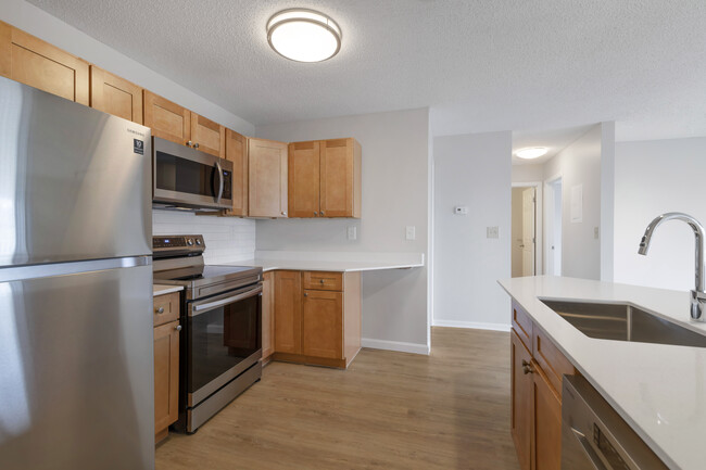 Renovated Package I kitchen with stainless steel appliances, white quartz countertops, maple cabinetry, white tile backsplash, and hard surface flooring - Avalon Burlington