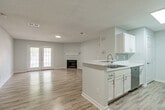 Located at 350 Byram Dr in Byram, Mississippi, this single-floor home offers a clean, modern aesthetic with a bright and open interior design. The open-concept living and dining area is anchored by a fireplace and flooded with natural light through French doors, which provide both an inviting focal point and outdoor access. Light wood-tone luxury vinyl plank flooring runs throughout the main living areas and hallways, creating a cohesive and contemporary feel.

The kitchen is thoughtfully designed in a galley style with crisp white shaker cabinetry, light quartz countertops, a tile backsplash, and stainless steel appliances including a range, microwave, and dishwasher. A peninsula with a sink connects the kitchen to the living space, ideal for casual dining or entertaining.

The bedroom features plush carpeting, a ceiling fan with light fixture, and a window that allows for natural light and ventilation. The bathroom is finished with wood-look tile flooring, white cabinetry with marble-look countertops, and a full tub-shower combination with a curved curtain rod and chrome fixtures.

A hallway connects the rooms and includes an electrical panel, adding functional convenience. Throughout the home, neutral gray walls, white trim, and recessed lighting contribute to a clean, move-in-ready atmosphere.