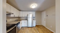 Located at 678 Princeton in Lowell, MA, this single-floor unit offers a practical and well-organized layout with a neutral color palette throughout. The kitchen serves as a functional highlight, featuring white shaker-style cabinetry with brushed nickel hardware, light granite countertops, and a full suite of stainless steel appliances including a refrigerator, electric range with overhead ventilation, and dishwasher. Wood-look flooring grounds the kitchen, giving it a clean, modern appearance.

The living area is generously proportioned, finished with wall-to-wall carpet in a warm beige tone and neutral walls. A sliding glass door allows natural light to fill the space while providing exterior access. Baseboard heating runs along the perimeter walls, and a wall-mounted air conditioning unit adds climate control convenience. The open sightline between the living area and kitchen creates a connected feel throughout the main living space.

The bedrooms are carpeted and simply finished, offering versatile layouts with access to natural light through windows fitted with vertical blinds. The bathroom is equipped with a full tub-shower combination, a white vanity with storage, and wood-look flooring, maintaining a cohesive and clean aesthetic consistent with the rest of the unit.