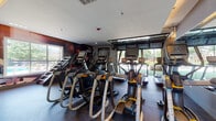 This fitness center is thoughtfully designed to accommodate a wide range of training styles, divided into distinct zones that flow seamlessly from one to the next. The cardio area is lined with a robust selection of Matrix treadmills, ellipticals, and stair climbers, all positioned to face a large glass garage door that rolls open to reveal views of the surrounding greenery, creating an energizing, open-air atmosphere during workouts. The strength training section is generously outfitted with cable machines, multi-functional racks, free weights, benches, and Motion Age functional training systems, all arranged to maximize space and usability. Bold yellow accent columns and wall-mounted mirrors amplify the sense of space while adding a dynamic visual energy to the interior. A rubberized, speckled floor runs throughout, providing traction and durability suited to high-intensity use. Motivational athletic murals and an inspirational quote painted along one wall contribute to the facility's energetic ambiance. A dedicated functional training area features a heavy tire for conditioning work, reinforcing the gym's commitment to comprehensive fitness offerings. Recessed and cove lighting keeps the space well-lit, while large windows and the retractable garage door ensure ample natural light throughout.