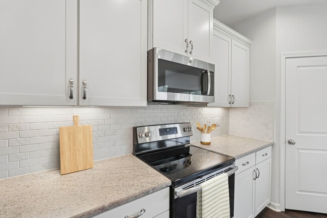 Upgrade Package kitchen with white cabinetry, designer tile backsplash, granite countertops, and stainless steel appliances - Avalon Townhome Collection Brier Creek
