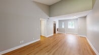 Located at 7648 Garners Ferry Rd in Columbia, SC, this one-bedroom, one-bathroom two-story unit offers a well-designed layout across two levels. The main living area is immediately welcoming, featuring soaring vaulted ceilings that lend an open, airy feel to the space, complemented by light-toned hardwood flooring that runs throughout. Natural light filters in through multiple windows, brightening the neutral gray walls and enhancing the overall sense of openness. The kitchen is appointed with white cabinetry, granite-look countertops, a stainless steel microwave, and an electric range, with ample counter and storage space arranged in a practical galley-style configuration. A closet is conveniently situated just off the kitchen area. The spacious bedroom features a ceiling fan with light fixture, a window with outdoor views of surrounding greenery, and direct access to a closet. The full bathroom includes a tiled tub-shower combination with chrome fixtures. Textured ceilings are present throughout the unit, adding a classic touch to the interior. Staircases connect the two floors, with the primary living spaces occupying the upper level. The clean, freshly finished interior presents a move-in-ready environment with a bright and functional ambiance.