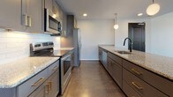 Located on Bainbridge Street in Richmond, Virginia, this two-story residence showcases a thoughtfully designed modern interior with high-quality finishes throughout. The main level features a generous open-plan living and dining area with dark hardwood-style flooring, recessed lighting, and a ceiling fan. Expansive floor-to-ceiling sliding glass doors and multiple large windows flood the space with natural light while offering views of the surrounding neighborhood. A staircase with a sleek black metal railing connects the two floors.

The kitchen is a standout feature, equipped with gray shaker-style cabinetry accented by gold hardware, granite countertops, a white subway tile backsplash, and a full suite of stainless steel appliances. A large central island with a matte black faucet and pendant globe lighting above adds both function and style. A convenient half bathroom with a granite-topped vanity is also found on this level.

Upstairs, the bedrooms feature hardwood-style flooring and ample natural light from well-placed windows with neighborhood views. The bathrooms are finished with gray cabinetry, granite vanity tops, matte black fixtures, and tile flooring. One bathroom includes a glass-enclosed walk-in shower with subway tile surround and a built-in bench, while another features a tub-shower combination, completing this well-appointed residence.