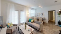 This well-appointed single-story residence offers a thoughtfully designed layout across several distinct living spaces. The open-concept kitchen serves as a functional centerpiece, featuring white shaker cabinetry, granite countertops, a peninsula with an undermount sink, pendant lighting, track lighting, and light wood-look flooring that extends throughout the main living areas. Appliances include a range, microwave, and full-size refrigerator.

The living and dining area is filled with natural light from multiple windows and a set of French doors, which provide an airy, open atmosphere. Light-colored walls and wood-look flooring create a cohesive, modern aesthetic throughout.

The primary bedroom is distinguished by a bold accent wall in warm yellow, complemented by carpeted flooring and a window with blinds and draping curtains. A second bedroom features neutral tones, carpeted flooring, and a bright window with outdoor views of greenery.

The bathroom includes granite countertops, white cabinetry, wood-look tile flooring, and ample mirror space. A dedicated laundry area houses a full-size side-by-side washer and dryer, adding everyday convenience. Hallways connect the spaces with clean, light-toned finishes throughout.