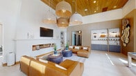 Located at 9111 Paragon Dr in Charlotte, NC, this thoughtfully designed single-floor community clubhouse spans a generous footprint, offering a refined and welcoming atmosphere throughout. The entry lobby immediately impresses with soaring ceilings clad in warm wood, a striking patterned terracotta tile floor, and a curved gold-accented reception desk. Large-scale landscape artwork adorns the walls, while floor-to-ceiling windows flood the space with natural light. A built-in mail center and a cozy window bench seat add practical elegance to the lobby area. The hallway connects seamlessly to the various spaces, featuring the same distinctive tile flooring and a curated gallery of artwork that guides visitors through the facility. The combined dining and living area is a standout, anchored by a substantial wooden dining table beneath an eclectic mix of pendant lights, complemented by a built-in shelving wall with decorative tile backing. The living room boasts soaring ceilings, light hardwood flooring, floor-to-ceiling windows with sheer drapery, a modern fireplace, and a shuffleboard table, creating an ideal social and recreational hub. Lush indoor plants, warm neutral tones, and a cohesive blend of natural materials — wood, tile, and woven textures — unify the space with an inviting, contemporary aesthetic.