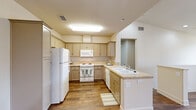This two-story, two-bedroom, two-bathroom home offers a thoughtfully organized layout spread across two levels. The main living floor features a combined kitchen and living room area, where warm hardwood-style flooring runs throughout. The kitchen is well-appointed with taupe cabinetry, light countertops, a full suite of white appliances including a refrigerator, electric range, built-in microwave, and dishwasher, all illuminated by a bright overhead skylight fixture. The open living area benefits from vaulted ceilings and ceiling fans, lending a sense of spacious airiness to the space. A carpeted staircase with a clean white handrail connects the levels. Both bedrooms feature plush carpeting, ceiling fans, and windows that invite natural light. The generously sized primary bedroom includes access to a private balcony and a dedicated closet. A walk-in closet with dual hanging rods provides ample storage. Each bathroom is finished with wood-look flooring, a vanity, and a tub-shower combination fitted with sliding glass doors and chrome hardware. Two hallways efficiently connect the home's rooms, and the overall palette of neutral creams and warm tones creates a cohesive, inviting ambiance throughout.