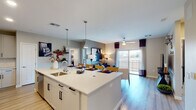 This well-designed single-floor residence offers a seamless blend of modern style and functional living across its thoughtfully arranged layout. The heart of the home is a striking open-concept kitchen, dining, and living area that flows effortlessly together. The kitchen is appointed with crisp white shaker cabinetry, quartz countertops, a large center island with bar seating and an undermount sink, stainless steel appliances, and a tasteful tile backsplash — all set above light hardwood flooring. Pendant lighting above the island adds a contemporary touch. The living area extends naturally from the kitchen, featuring a ceiling fan and large sliding glass doors that open to a private balcony, allowing an abundance of natural light and outdoor views. The primary bedroom is a comfortable retreat with plush carpeting, a ceiling fan, and a bold accent wall. Its en-suite bathroom offers a wide quartz vanity with white cabinetry, illuminated mirror, and a walk-in closet. A second bedroom mirrors the same cozy, carpeted comfort with ample natural light. The second bathroom echoes the same refined finishes, featuring matching white cabinetry and quartz surfaces. Neutral tones throughout create a cohesive, welcoming ambiance.