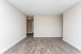 Located at 3838 Lyons St in Macon, Georgia, this single-story property offers a straightforward, functional layout across several well-defined living spaces. The living areas are finished with durable wood-look flooring in a warm, medium-toned hue, providing a cohesive look throughout the main spaces. Natural light filters in through multiple windows, contributing to a bright and open atmosphere.

The kitchen is equipped with white cabinetry spanning both upper and lower sections, complemented by granite-style countertops along an L-shaped layout. A stainless steel sink is positioned beneath additional cabinet storage, and the space connects naturally to the adjoining living and dining areas, as seen in the overhead floor plan view.

The living room is generously proportioned, featuring the same wood-look flooring and neutral beige walls. A large window along one wall allows ample natural light and provides views of the surrounding neighborhood. A wall-mounted air conditioning unit is also present in this room.

The bedroom is carpeted and finished with the same neutral palette, offering a window that brings in natural light. The bathroom is notably detailed, featuring large-format, earth-toned stone-look tiles covering the walls surrounding a full soaking tub, with a window positioned above for natural light. Clean white fixtures complete the space.