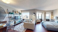 Located at 441 East Erie Street in Chicago's sought-after Streeterville neighborhood, this studio residence offers a thoughtfully designed open-plan layout finished with warm hardwood flooring throughout. The main living area serves as the heart of the unit, seamlessly combining living, sleeping, and dining functions into a cohesive, well-utilized space. Large windows frame sweeping views of the Chicago skyline and Lake Michigan, flooding the room with natural light. A lean-to shelving unit provides stylish storage and display space alongside the entertainment area, while a comfortable seating arrangement anchors the living zone. The sleeping area is positioned adjacent to the living space, with a generous closet offering practical storage. A pass-through opening connects to the kitchen, which features warm wood cabinetry, under-cabinet lighting, and full appliances. Two hallways provide a sense of entry and separation within the open layout, with wall art and a patterned runner adding character. The bathroom is well-appointed with rich wood vanity cabinetry, a marble-style countertop, a large mirror, and a tiled shower. A textured ceiling adds architectural interest throughout. This compact yet complete studio delivers an efficient urban living experience in a prime Chicago location.