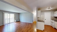 This single-floor residence offers a practical and comfortable layout with warm hardwood flooring extending throughout the main living areas, bedrooms, and kitchen. The open-concept design connects the living room and kitchen, creating a spacious, cohesive flow ideal for everyday living and entertaining. The living room is generously sized with soft gray walls, a ceiling fan, and a sliding glass door that brings in natural light and provides access to the outdoors. A wall-mounted HVAC unit ensures year-round comfort. The kitchen is well-appointed with white cabinetry, dark granite countertops, a decorative stacked-tile backsplash, a stainless steel sink, and white appliances including a range, dishwasher, and refrigerator. A peninsula with a breakfast bar visually separates the kitchen from the living space while maintaining the open feel. The bedrooms are bright and airy, each featuring hardwood floors, soft neutral walls, and windows that frame views of the surrounding greenery. The bathroom includes a full soaking tub and shower combination with classic tiled surround in cream and brown tones. Overall, the space presents a clean, neutral palette that is move-in ready and easily personalized.