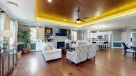 Located at 101 Cambridge Ln in Newtown, PA, this thoughtfully designed single-floor space combines refined style with functional living across an open, well-proportioned floor plan.

The kitchen and living area form the heart of the space, unified by rich hardwood flooring that flows seamlessly throughout. The kitchen is outfitted with crisp white cabinetry, stainless steel appliances, a tile backsplash, and a central island with a bright white countertop and seating for multiple guests. Dual pendant lights overhead add warmth and definition to the cooking and dining zone, while crown molding and recessed lighting contribute a polished, finished look.

The living room is a standout, anchored by a stacked stone fireplace flanked by built-in shelving and cabinetry. A dramatic tray ceiling with ambient LED uplighting creates a warm golden glow, complemented by a ceiling fan and recessed lighting. Multiple windows invite natural light, while elegant drapery adds softness to the room. Built-in shelving provides both display and storage opportunities.

The office is accessed through a glass-paned French door, offering a quiet, defined workspace with views into the broader living area. An entry area with hardwood floors and generous ceiling height completes the layout, reinforcing the open and airy character of this well-crafted space.
