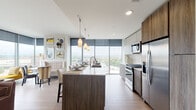 Located on Euclid Avenue in the heart of Cleveland, this contemporary residence is defined by its striking floor-to-ceiling window walls that frame panoramic views of the city skyline and surrounding urban landscape. Light wood-tone flooring runs throughout the open-concept living areas, reinforcing the clean, modern aesthetic present across the entire unit.

The kitchen is a standout feature, equipped with stainless steel appliances including a gas range, built-in microwave, and refrigerator. Flat-front cabinetry in both white and warm wood tones lines the walls, while a large island with a light stone countertop provides seating and additional workspace. Pendant lighting overhead adds a refined touch. The living and dining areas flow naturally from the kitchen, benefiting from corner window walls that maximize natural light and city views.

The primary bedroom features a bold textured accent wall, floor-to-ceiling windows, and soft carpeting, creating a comfortable retreat. Additional bedrooms include closet storage and access to natural light. Two full bathrooms are finished with wood-toned vanities, white quartz countertops, and light tile flooring, with one featuring a subway-tiled soaking tub and shower combination. Throughout, the design balances contemporary finishes with a warm, inviting ambiance.