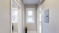 Located at 34 E Milwaukee Street in Detroit's vibrant New Center neighborhood, this one-bedroom, one-bathroom unit offers a well-organized layout across a single floor. The spacious bedroom is the standout feature of the unit, showcasing warm hardwood floors, soft gray walls with crisp white crown molding, and multiple windows that invite abundant natural light and views of the surrounding cityscape. A ceiling fan provides year-round comfort, while a classic cast-iron radiator adds a nod to the building's historic character. A charming five-panel wooden door leads from the bedroom into the bathroom, adding a distinctive architectural touch. The kitchen is compact yet fully functional, outfitted with white cabinetry, a gas range, stainless steel microwave, and light tile flooring. A window above the counter brings in natural light. The bathroom features floor-to-ceiling large-format white tiles surrounding a soaking tub, creating a clean and modern aesthetic. The unit also includes a hallway, closet, and dedicated entry area, making efficient use of the available space. The combination of classic building details and updated finishes gives this unit a balanced blend of historic Detroit character and modern livability.