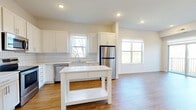 Located at 251 Eldorado Dr in Jordan, MN, this 2-bedroom, 2-bathroom unit offers a clean, modern aesthetic throughout its well-planned single-floor layout. Light wood-tone flooring runs continuously through the living areas and bedrooms, complementing the bright, neutral color palette.

The kitchen is a standout feature, appointed with white shaker-style cabinetry extending to the ceiling, a chevron-patterned tile backsplash, stainless steel appliances including a refrigerator, range, microwave, and dishwasher, and a central island that adds both workspace and visual appeal. Multiple windows fill the kitchen and adjacent living area with natural light, while a sliding glass door opens to a private balcony overlooking natural surroundings.

Both bedrooms are well-proportioned and bright, each featuring large windows that frame views of the wooded landscape. Closets with double doors provide ample storage in each room. The bathrooms are finished with clean, simple fixtures including a walk-in shower with white surround and chrome hardware. A dedicated utility room and three closets throughout the unit contribute to practical, organized living. Recessed lighting and a neutral, move-in-ready finish complete this functional and inviting space.