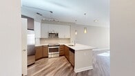 This contemporary 680 square foot apartment offers a well-designed living space with two bedrooms and one bathroom. The open-concept layout maximizes the use of space, creating a seamless flow between the living area and kitchen. The kitchen is a highlight, featuring modern stainless steel appliances, including a refrigerator, stove, and built-in microwave. Sleek cabinetry in a two-tone design of white and wood finishes provides ample storage and adds visual interest.

The primary bedroom, measuring 170 square feet, offers a generous space for rest and relaxation. Both bedrooms feature plush carpeting for comfort underfoot. The bathroom is equipped with a modern white bathtub and shower combination, complemented by clean, white tiling.

Throughout the apartment, large windows allow natural light to flood the space, creating a bright and airy atmosphere. The living areas boast stylish wood-look flooring, adding warmth and durability to the space. For added convenience, the unit includes an in-unit laundry area with a top-loading washing machine.

The neutral color palette of light grey walls and white trim provides a versatile backdrop for various decor styles. The apartment's layout and amenities make it an ideal choice for those seeking a comfortable and efficient urban living space.