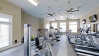 This fitness center offers a comprehensive workout environment designed to support a range of exercise routines. The space is outfitted with an extensive selection of strength-training machines, including cable and resistance equipment, as well as cardio machines such as ellipticals and steppers positioned along the perimeter. A stability ball and additional free-standing equipment round out the strength-training options.

Natural light fills the room through a row of large windows along one wall, creating a bright and energizing atmosphere. Multiple ceiling fans are evenly distributed throughout, promoting air circulation and comfort during workouts. The flooring features a durable, neutral-toned surface suited for high-traffic fitness use.

The walls are finished in a warm beige tone, contributing to a clean and welcoming aesthetic. Recessed and flush-mounted lighting supplements the natural light, ensuring the space remains well-lit at all hours. The open layout allows for easy movement between equipment, providing an uncluttered and functional environment for users of all fitness levels.