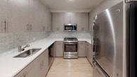 This single-floor unit offers two bedrooms, two full bathrooms, and a versatile den across a thoughtfully designed layout. The open living area features light hardwood flooring that extends through the main spaces, recessed lighting, and a pendant light fixture. The kitchen is well-appointed with gray cabinetry, a mosaic tile backsplash, white quartz-style countertops, and a full suite of stainless steel appliances including a gas range, microwave, and refrigerator. A dedicated laundry closet with a stacked washer and dryer is conveniently located off the main living area. Both bedrooms are carpeted and generously sized, each offering closet space. One bedroom features a walk-in closet, while another benefits from two windows that bring in natural light and outdoor views. The den provides additional flexible space with soft carpet flooring. Both bathrooms are finished with large-format tile flooring, wood-toned vanities with white countertops, and mirrored medicine cabinets. Clean neutral walls and consistent finishes throughout give the unit a cohesive, modern aesthetic.