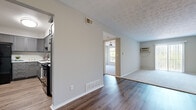 This single-floor unit offers a thoughtfully laid-out interior with a blend of hardwood-style and carpeted flooring across its various rooms. The open living area is bright and airy, featuring a textured ceiling, neutral gray-toned walls, and a wall-mounted air conditioning unit alongside floor-level vents for year-round comfort. A sliding glass door dressed with vertical blinds allows natural light to pour in while providing outdoor access.

The kitchen is a standout space, designed with ample gray shaker-style cabinetry, light countertops, and a full suite of black appliances including a gas range and a full-size refrigerator. Light wood-style flooring and clean white walls give the kitchen a modern, functional feel.

The bedrooms are generously sized, each equipped with ceiling fans for added ventilation. One bedroom features plush carpeting and a wide window framing views of surrounding greenery, creating a calm and comfortable retreat. Another bedroom offers hardwood-style flooring, a sliding-door closet, and direct access to an entry door. Additional rooms feature soft carpet and clean, neutral finishes throughout.

The textured ceilings and consistent neutral palette across the unit create a cohesive, understated aesthetic, providing a versatile canvas well-suited to a variety of interior styles.