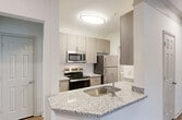 This contemporary apartment offers a thoughtfully designed living space with an open floor plan. The main living area showcases gleaming hardwood floors and is illuminated by a stylish ceiling fan with integrated lighting. French doors lead to a private balcony or patio, allowing natural light to flood the space.

The kitchen is a highlight, boasting sleek light-colored cabinetry, stainless steel appliances, and elegant granite countertops. A convenient breakfast bar provides additional seating and workspace.

The bedroom areas are generously sized, with plush carpeting for comfort. Large windows offer plenty of natural light, and built-in closets provide ample storage. The bathroom features modern fixtures, including a tub-shower combination with safety bars, and a vanity with a granite countertop.

Additional amenities include in-unit laundry facilities and central air conditioning. The neutral color palette throughout creates a calm and inviting atmosphere, allowing residents to easily personalize their space. This well-appointed apartment combines functionality with contemporary style, offering a comfortable and attractive living environment.