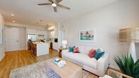 This thoughtfully designed 2-bedroom, 2-bathroom residence offers a bright, open-concept floor plan with a coastal-inspired aesthetic. The living room is a comfortable gathering space featuring light wood flooring, a ceiling fan, and large windows dressed in neutral drapes and blinds that invite generous natural light. It flows seamlessly into the kitchen, which is outfitted with crisp white cabinetry extending to the ceiling, stainless steel appliances, a subway tile backsplash, and a wood-accented island with built-in shelving and bar seating—ideal for casual dining or entertaining. A dedicated laundry area and entrance hallway add practical convenience. The primary bedroom is a well-sized retreat with plush carpeting, a ceiling fan, and a large window offering outdoor views. The second bedroom features sliding glass doors that open directly onto a private balcony overlooking the resort-style community courtyard. Both bathrooms are finished in large-format white tile with modern floating vanities and clean, minimalist fixtures—one featuring a soaking tub with shower. Each bedroom is complemented by a dedicated closet. The overall ambiance is light, airy, and contemporary, with a consistent neutral palette and warm wood accents throughout.