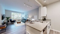 Located at 5648 Bay St in Emeryville, CA, this one-bedroom, one-bathroom residence offers a thoughtfully designed open-concept layout with modern finishes throughout. The combined kitchen and living area serves as the heart of the home, featuring wood-look luxury vinyl flooring, neutral walls, and large windows that invite ample natural light and views of surrounding greenery. The kitchen is equipped with stainless steel appliances — including a refrigerator, range, and over-the-range microwave — complemented by white shaker cabinetry, a stainless steel sink, and a peninsula with bar seating for two. Adjacent to the kitchen, a dedicated workspace nook with room for a desk provides a functional area for remote work. The living room offers generous space with track lighting overhead and a comfortable, airy ambiance. The bedroom features soft carpeting, a neutral color palette, framed wall art, and direct access to both a walk-in closet and the full bathroom. A sliding glass door in the bedroom opens to the outside, enhancing ventilation and light. The bathroom includes a combination tub and shower, a white vanity, and matching wood-look flooring that ties the space together cohesively.