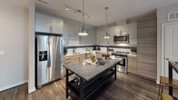 This single-floor residence showcases a contemporary design with a thoughtful layout. The kitchen serves as a central highlight, featuring high-gloss upper cabinetry paired with wood-tone lower cabinets, white subway tile backsplash accented by a distinctive black mosaic tile border, and stainless steel appliances including a range, microwave, and dishwasher. A granite-topped island with pendant lighting anchors the space, which flows into the open living area finished with dark hardwood-style flooring and track lighting. Sliding glass doors connect the living area to a private balcony, filling the space with natural light.

Both bedrooms are carpeted and fitted with ceiling fans, each offering direct balcony access through sliding doors. The two bathrooms maintain a consistent modern aesthetic, featuring large-format light tile flooring, dark espresso vanity cabinetry with white countertops, and oversized mirrors. The primary bath includes a walk-in tiled shower with a matching mosaic accent border, while the secondary bath provides a clean, functional layout. Both bedrooms are complemented by generous walk-in closets equipped with adjustable wire shelving systems, providing ample storage throughout.