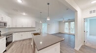 Located at 23 Evolve Parkway in Palm Coast, Florida, this well-appointed 2-bedroom, 2-bathroom single-floor residence offers a clean, modern aesthetic throughout. The open-concept layout seamlessly connects the kitchen, dining, and living areas, creating a bright and airy communal space. The kitchen is a standout feature, showcasing white shaker cabinetry, dark granite-style countertops, stainless steel appliances, and a large center island with pendant lighting and an undermount sink — ideal for both cooking and entertaining. Light wood-look flooring flows through the main living areas, complementing the crisp white walls and neutral palette. The living room opens to the outdoors through glass French doors, allowing generous natural light to fill the space. Both bedrooms are carpeted and feature ceiling fans, with the primary bedroom offering a walk-in closet with built-in wire shelving. The primary bathroom is well-equipped with a double vanity, dark countertops, white cabinetry, and a glass-enclosed walk-in shower. The second bathroom mirrors the same refined finishes. Additional conveniences include a dedicated laundry area, a pantry, and multiple closets throughout, providing ample storage.