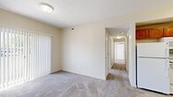 Located in Taylorsville, Utah, this two-bedroom, one-bathroom single-floor residence offers a functional and efficiently organized layout. The living area features neutral beige walls, plush carpeting, and large vertical-blind-covered sliding doors that allow natural light to filter in. A central hallway connects the main living spaces, leading to two well-proportioned bedrooms. Each bedroom is finished with soft carpet, neutral tones, and windows with blinds that bring in natural light and outdoor views. The primary bedroom includes a closet with a bi-fold door and a dedicated hanging rod for storage. The kitchen is equipped with warm, medium-toned wood cabinetry, granite-look countertops, a double sink, a white dishwasher, white appliances, and light wood-look vinyl flooring, providing a clean and practical cooking space. The bathroom features wood-look tile flooring, a tub-shower combination with tile surround and a handheld showerhead, and accessibility-friendly grab bars. Additional spaces include a utility room, a closet, and two entrance areas. The overall design is clean and straightforward, with consistent neutral finishes throughout that create a cohesive and move-in ready environment.