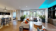 Located at 12850 SW Ash Ave in Tigard, Oregon, this thoughtfully designed single-floor community space offers a welcoming blend of modern aesthetics and functional living areas. The open-concept layout incorporates a kitchen, living room, and dining room, all unified by polished concrete flooring that lends the space an urban, contemporary character.

The kitchen is outfitted with sleek, light-wood cabinetry, white quartz countertops, a classic tile backsplash, and stainless steel appliances including a range, wine refrigerator, and built-in microwave. Dark open shelving above provides both storage and display space, adding visual depth to the design. Adjacent to the kitchen, the dining area features a substantial natural wood table paired with dark Windsor-style chairs, anchored by a sculptural wire pendant light overhead.

The living room area is highlighted by a built-in platform bench with upholstered cushions and accent pillows, positioned beneath oversized windows that flood the space with natural light and frame views of the lush courtyard below. A striking woven pendant fixture serves as a focal point in the lounge nook.

The entry lobby opens directly to a beautifully landscaped outdoor courtyard, complete with brick paver walkways, mature trees, flowering shrubs, and seating areas — creating a seamless indoor-outdoor experience.