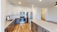Located at 336 Chestnut Pkwy in Indian Trail, NC, this single-story home showcases a clean, modern design with thoughtful finishes throughout. The kitchen is a standout feature, equipped with stainless steel appliances including a refrigerator, range, microwave, and dishwasher. White upper cabinetry is paired with gray lower cabinets, complemented by a classic white subway tile backsplash and granite countertops that extend to a spacious kitchen island — ideal for both meal preparation and casual dining. Warm-toned hardwood-style flooring flows through the kitchen and main living areas, while a glass door provides access to an outdoor area and allows natural light to fill the space. The bedrooms are carpeted for comfort, each featuring a ceiling fan with light and windows fitted with horizontal blinds that offer privacy while admitting natural light. The bathroom is well-finished with a granite-topped vanity, matte black hardware and fixtures, a subway tile-surround soaking tub, and wood-style flooring. Additional highlights include a walk-in closet with built-in wire shelving, recessed lighting throughout, and a consistent neutral color palette that gives the entire home a bright, cohesive aesthetic.