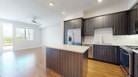 Located at 13385 Highlands Pl in the desirable Carmel Valley neighborhood of San Diego, this single-floor residence showcases a clean, contemporary design with thoughtfully selected finishes throughout. The open-concept kitchen serves as a central highlight, featuring dark wood-grain cabinetry extending to the ceiling, stainless steel appliances including a French door refrigerator, gas range, built-in microwave, and dishwasher. A white subway tile backsplash adds texture against the dark cabinetry, while a large island with a light quartz countertop provides additional workspace and casual seating. Warm-toned hardwood flooring flows through the kitchen and living areas, complemented by recessed lighting and a ceiling fan. The bedroom areas include both carpeted and hardwood-floored rooms, each filled with natural light from generously sized windows that frame outdoor greenery and open sky views. One bedroom offers direct access to a balcony, extending the living space outdoors. A walk-in closet adds practical storage to the sleeping quarters. The bathroom features a soaking tub with tile surround, dark wood vanity with quartz countertop, and large-format tile flooring, maintaining the modern aesthetic found throughout the residence.