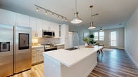 Located in Melbourne, FL, this well-appointed one-bedroom, one-bathroom residence offers a thoughtfully designed open-concept layout with light wood-look flooring throughout. The combined living, dining, and kitchen area forms the heart of the home, featuring a large center island with quartz countertops, a deep undermount sink with a professional-style faucet, and a full suite of stainless steel appliances including a French door refrigerator, gas range, and built-in microwave. White shaker cabinetry with a subway tile backsplash, track and pendant lighting, and a sliding barn door accent add modern character to the space. The dining area accommodates a full-sized table and benefits from natural light through large windows. The generously sized primary bedroom includes a ceiling fan, ample natural light, and access to a well-organized walk-in closet with custom shelving. The bathroom features a single vanity with quartz countertops, wood-look tile flooring, and a glass-enclosed shower. Additional highlights include three closets, a dedicated laundry area, a utility room, a hallway, and a private balcony — offering comfortable, functional living in a clean, contemporary setting.