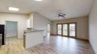 This single-floor residence offers a thoughtfully designed open-concept layout that seamlessly connects the kitchen and living areas. The kitchen is a standout feature, equipped with stainless steel appliances, granite countertops, two-tone cabinetry with white upper and gray lower cabinets, and a peninsula that provides additional prep space and serves as a natural divider between the kitchen and living area. Light wood-look flooring runs consistently throughout the entire unit, creating a cohesive and clean aesthetic.

The living area benefits from vaulted ceilings and a ceiling fan, enhancing the sense of openness. A set of large glass doors floods the space with natural light and provides outdoor access. The bedrooms are comfortably sized, each featuring a ceiling fan, windows with blinds, and the same light wood-look flooring. The bathrooms are finished with granite-topped vanities, white tile tub-shower combinations, and brushed nickel fixtures and grab bars. A dedicated in-unit laundry room accommodates a full-size washer and dryer with additional wire shelving for storage. The entry foyer offers a clean transition into the home. Overall, the space presents a bright, neutral palette with modern finishes throughout.