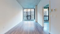 Located at 375 Rue de la Concorde in the heart of Montréal, this 2-bedroom, 1-bathroom unit delivers a contemporary urban aesthetic throughout its well-organized single-floor layout. The living room is a bright, open space anchored by large black-framed floor-to-ceiling windows that fill the room with natural light and offer views of the surrounding cityscape. Exposed concrete ceilings lend an industrial edge, while light hardwood flooring adds warmth and continuity throughout the common areas. The kitchen is sleek and functional, featuring a full suite of stainless steel appliances — including a refrigerator, range, microwave, and dishwasher — paired with dark cabinetry, glossy upper cabinets, a subway tile backsplash, and a dark countertop. Both bedrooms are finished with hardwood-style flooring and clean white walls. The primary bedroom benefits from a dedicated closet with full-panel bifold doors, while the second bedroom features a tall, narrow black-framed window that draws in natural light. The bathroom is finished in a crisp, modern style with large-format floor tiles, a soaking tub with subway tile surround, a wall-mounted vanity with an integrated sink, and a mirrored medicine cabinet. A hallway and additional closet complete the layout, providing practical storage throughout.