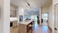 This thoughtfully designed one-bedroom, two-bathroom residence in Huntsville, Alabama offers a modern open-concept layout with stylish finishes and efficient use of space. The kitchen serves as a focal point, anchored by a large granite-topped island with a built-in sink and bar seating, complemented by warm wood-tone cabinetry, under-cabinet lighting, stainless steel appliances, and light hardwood flooring that flows throughout the main living areas. A pendant light and linear overhead fixture add a contemporary touch above the island and prep areas. The open living room benefits from abundant natural light streaming through floor-to-ceiling sliding glass doors, which lead to an outdoor area with open views. A ceiling fan and clean neutral walls complete the airy, welcoming atmosphere. The bedroom is a serene retreat with plush carpet, a ceiling fan, and a large window framing outdoor greenery. A distinctive sliding barn door opens to the en-suite bathroom, which features a granite vanity, wood-tone cabinetry, a soaking tub, and a tiled walk-in shower. A spacious walk-in closet with wire shelving provides generous storage. The second bathroom offers additional convenience, rounding out this well-appointed Huntsville residence.