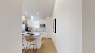 This well-designed single-story home offers two bedrooms, one bathroom, and a thoughtfully crafted open-concept floor plan that maximizes both space and functionality. The living room immediately impresses with soaring vaulted ceilings, light hardwood-style flooring, and a ceiling fan overhead. French doors flood the space with natural light while providing outdoor access, creating an airy and welcoming atmosphere.

The kitchen and living area flow seamlessly together, anchored by a generous island featuring a striking granite countertop and bar seating illuminated by elegant pendant lights. White shaker cabinetry, a white subway tile backsplash, stainless steel appliances, and dark countertops complete the kitchen's modern aesthetic. A built-in wine rack adds a distinctive design touch.

The spacious primary bedroom features plush carpeting, a ceiling fan, and multiple windows that invite ample natural light and outdoor views. Two closets provide generous storage throughout the home. The bathroom is clean and functional, offering a combined tub and shower, a white vanity with dark countertop, and brushed gold hardware accents.

Throughout the home, a crisp white palette, warm wood-toned flooring, and carefully considered details create a cohesive, modern, and inviting living environment.