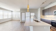 This single-floor residence offers a well-designed open-concept layout that seamlessly connects the kitchen, dining, and living areas. The kitchen is a standout feature, equipped with dark-toned shaker-style cabinetry, stainless steel appliances including a French door refrigerator, electric range, and built-in microwave. A subway tile backsplash complements the crisp white quartz countertops, which extend to a generous island with a stainless steel undermount sink and pendant lighting above. Light wood-style flooring runs throughout the main living areas, enhancing the bright, airy feel created by multiple windows dressed with horizontal blinds. The living space benefits from a ceiling fan and track lighting, and a door provides access to an outdoor area. A built-in arched shelving nook adds a practical storage element near a secondary living space. The bedrooms are carpeted for comfort, with the primary bedroom offering direct access to a dedicated bathroom and a spacious walk-in closet with built-in shelving and hanging rods. The bathroom features dark vanity cabinetry with a white countertop, wood-look flooring, and a tiled tub-shower combination. Additional carpeted rooms provide flexible living options throughout this clean, modern space.